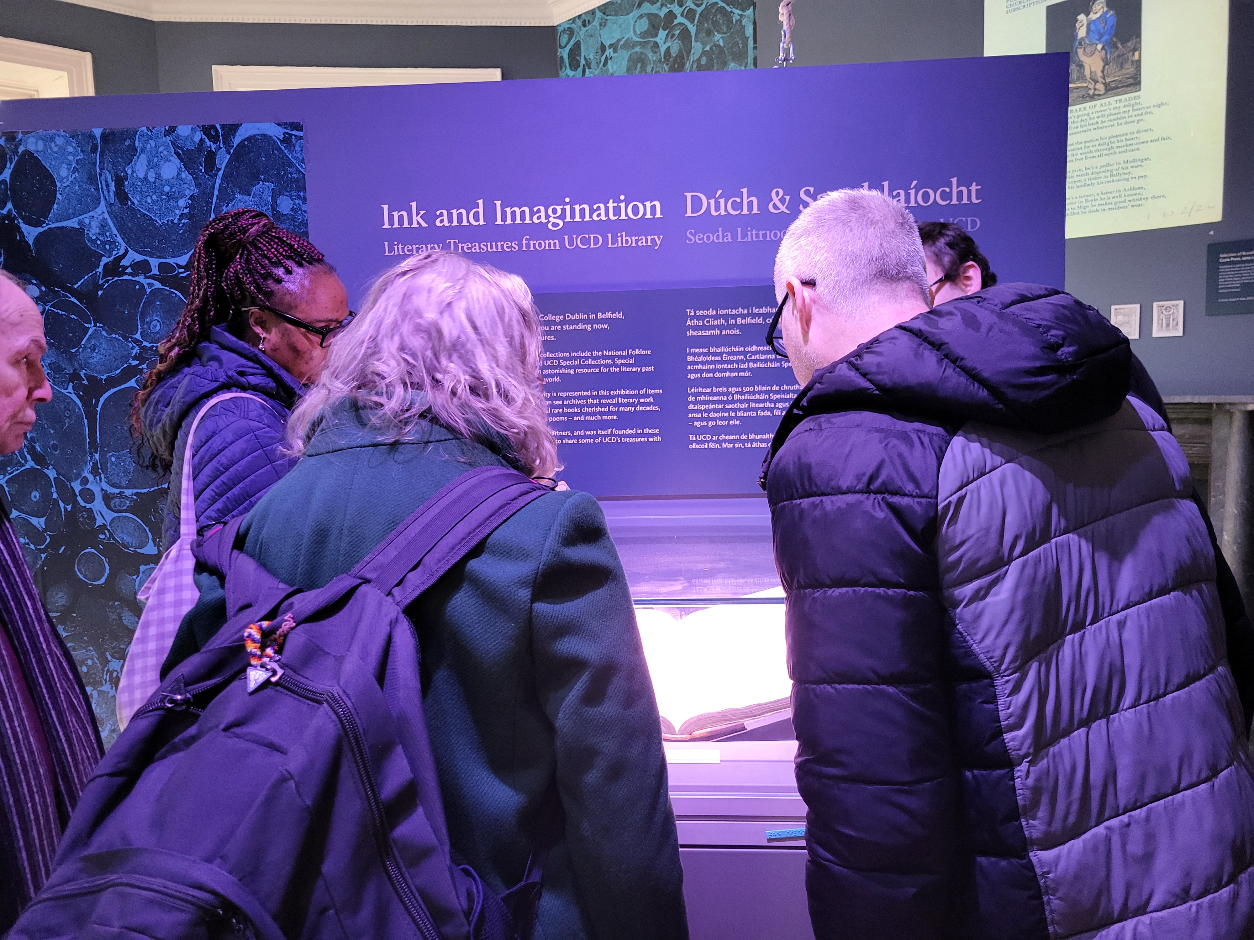 People lean over a book with a purple display in the background which reads 