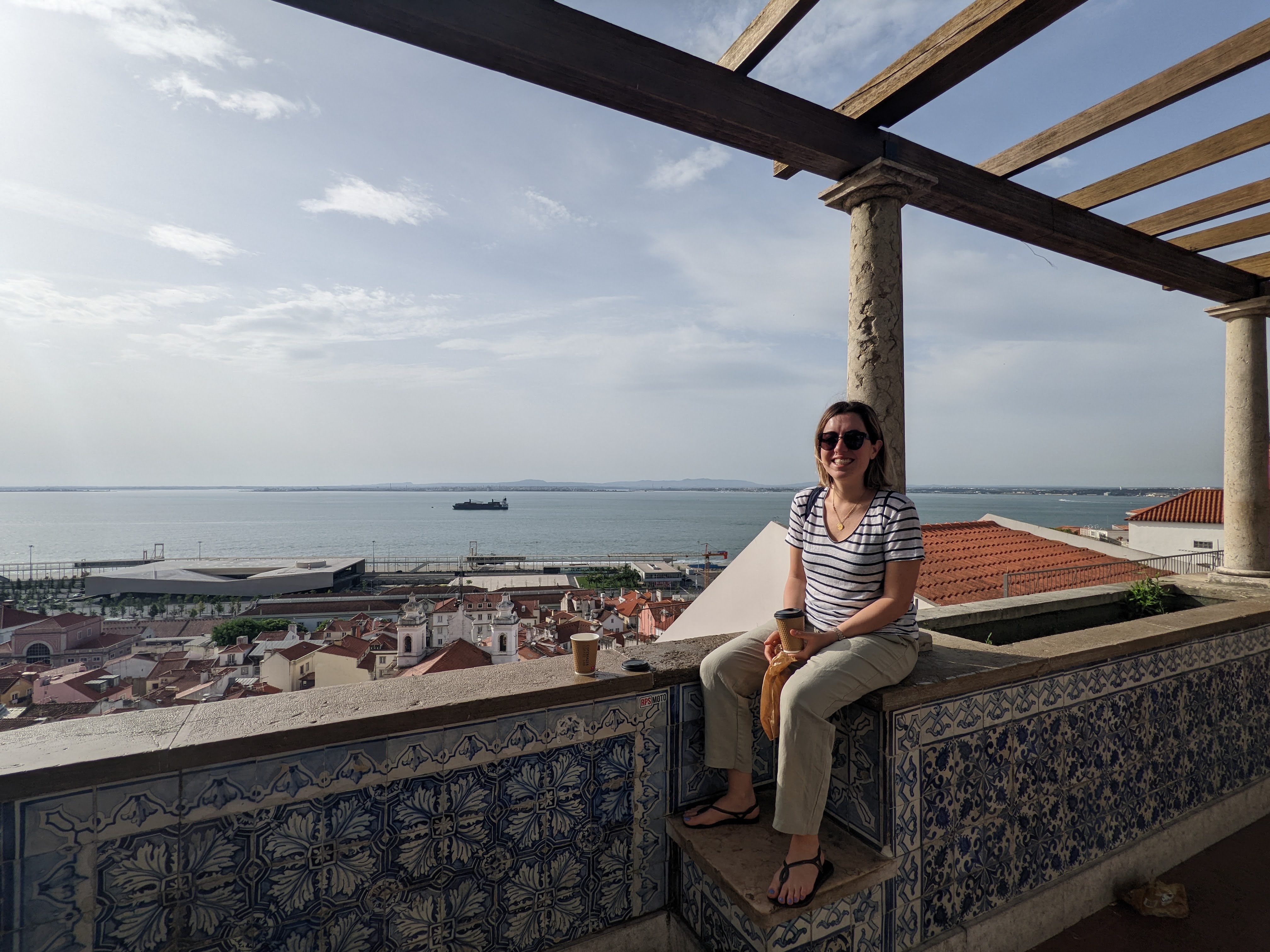 AONTAS EU Projects Officer Ecem Akarca sitting on a balcony with a blue sky and blue sea and city in the background