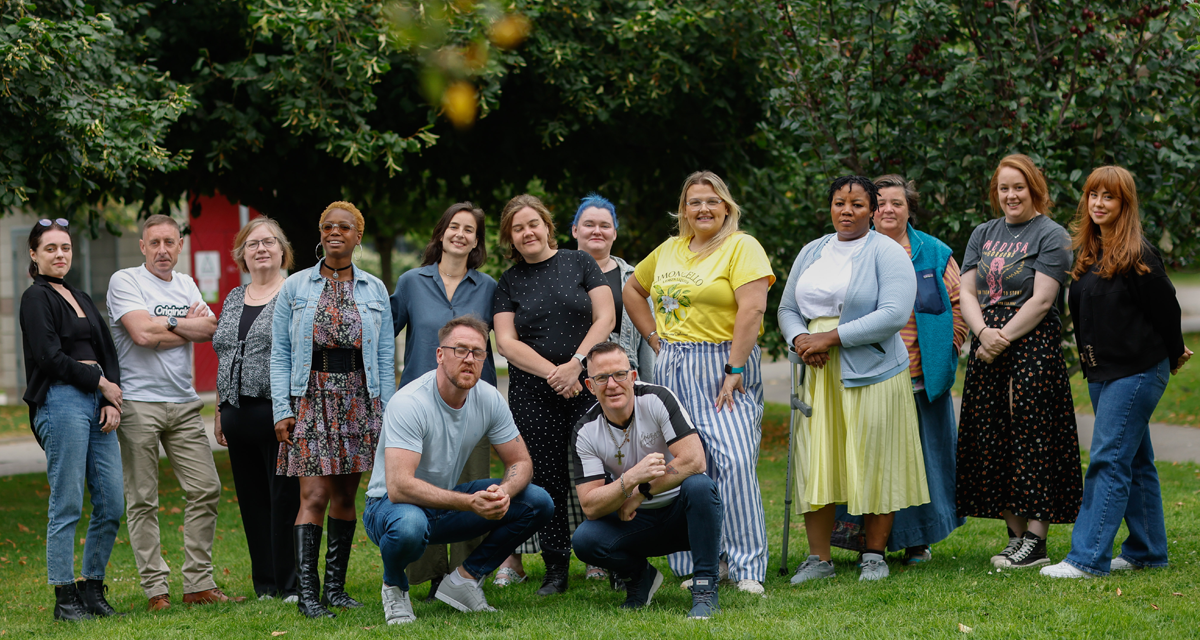 A diverse group of community education learners stand together posing and laughing while promoting the Community Education 2025 campaign
