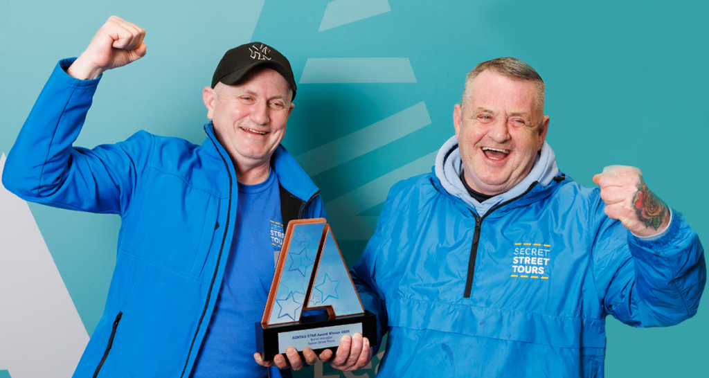 Two tour guides from Secret Street Tours cheer with fists in the air holding up their STAR Award statuette