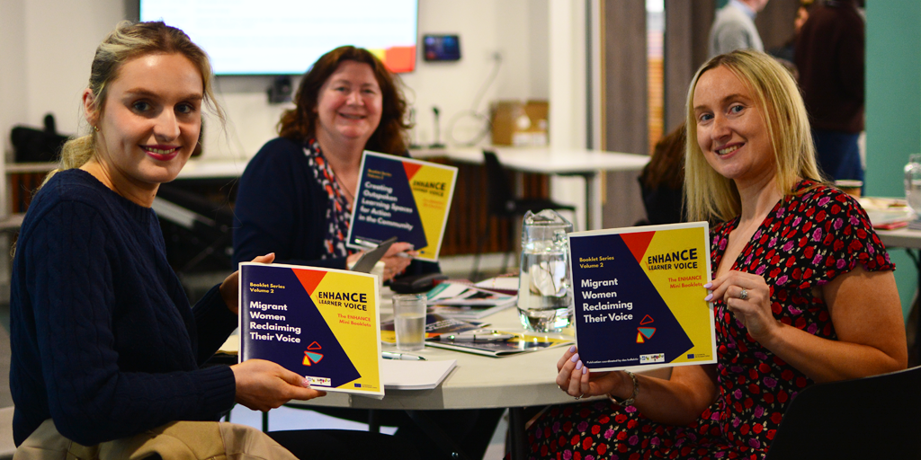 Participants at the Enhance event hold up booklets on Migrant Women Reclaiming Their Voice